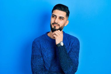 Sakallı, sıradan bir kazak giyen yakışıklı bir adam ciddi bir yüz ifadesi olan eli çeneli bir soru soran, kafa karıştırıcı bir fikir hakkında düşünceli biri. 