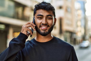 Genç Arap adam gülümsüyor, kendinden emin bir şekilde caddedeki akıllı telefondan konuşuyor.