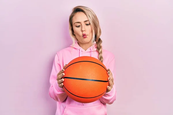 漂亮的金发碧眼的年轻女子手握篮球 用嘴和眼神做鱼脸 疯狂而滑稽 — 图库照片