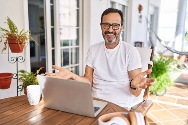 自宅でコンピュータのラップトップを使用している中世の男は 友好的な歓迎 肯定的かつ自信を持って挨拶としてオープン腕で陽気に笑顔 — ストック写真
