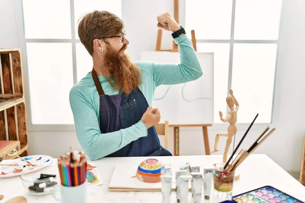 红头发男人 留着长胡子 在艺术工作室里画着黏土碗 露出胳膊肌肉 露出自豪的笑容 健身概念 — 图库照片
