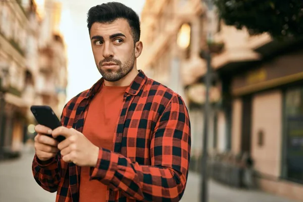 Joven Hombre Hispano Con Expresión Seria Usando Smartphone Ciudad —  Fotos de Stock
