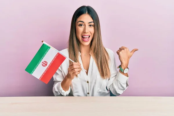 Fiatal Spanyol Kezében Irán Zászló Asztalon Mutatva Hüvelykujját Oldalra Mosolyogva — Stock Fotó