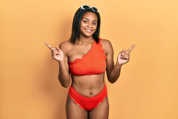 身穿比基尼的年轻的非洲裔美国女孩带着自信的微笑 手指指向不同的方向 复制广告空间 — 图库照片