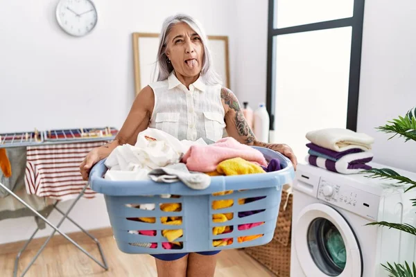 中年白髪の女が洗濯籠を持っている舌を突き出して幸せと面白い表情 — ストック写真