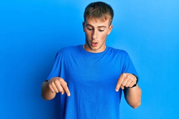 年轻的高加索人 身穿休闲的蓝色T恤 手指垂下 露出广告 惊讶的脸和张开的嘴 — 图库照片