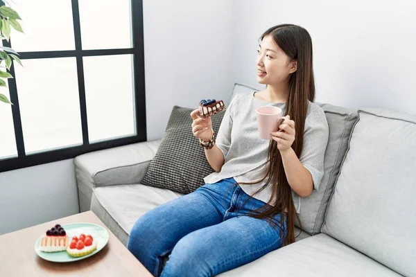 Young Asian Woman Eating Pastries Sitting Sofa Living Room — Stockfoto