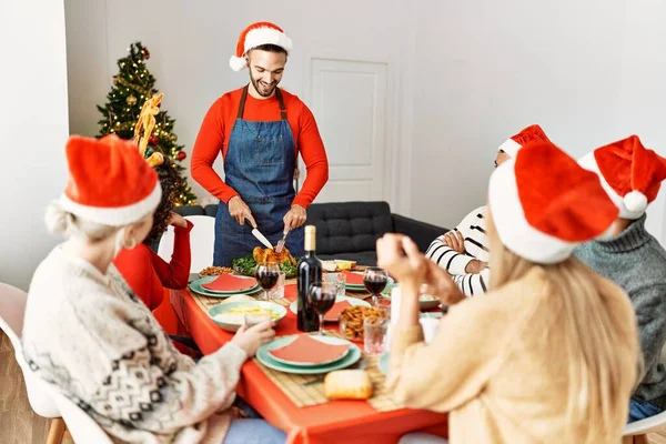 若い人たちのグループは 幸せなクリスマスディナーを持って笑って 男は自宅で提供するロースト七面鳥を切断 — ストック写真