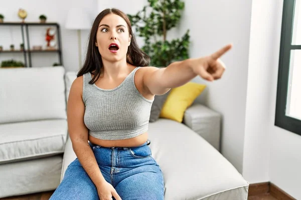 Jonge Brunette Vrouw Zitten Bank Thuis Wijzen Met Vinger Verrast — Stockfoto