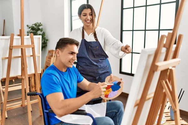 Öğretmen ve engelli boyacı. Tekerlekli sandalyede oturmuş resim yaparken gülümsüyor..