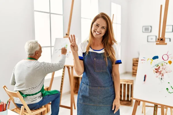西班牙裔女人穿着围裙出现在艺术工作室 用第三只手指头指指点点 面带微笑 自信而快乐 — 图库照片