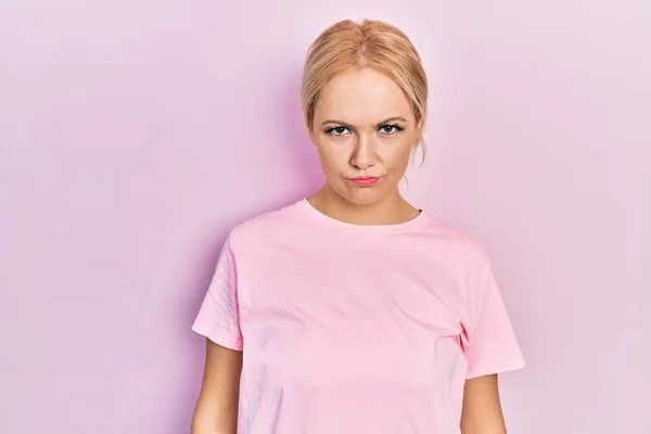年轻的金发女人穿着宽松的粉色T恤 疑神疑鬼 神经质 因为问题而皱着眉头 消极的人 — 图库照片