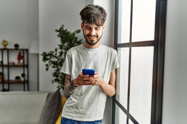 年轻的惊慌失措的男人在家里用智能手机自信地微笑 — 图库照片