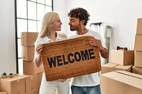 年轻漂亮的夫妇高兴地微笑着 在新家拿着欢迎的门垫 — 图库照片