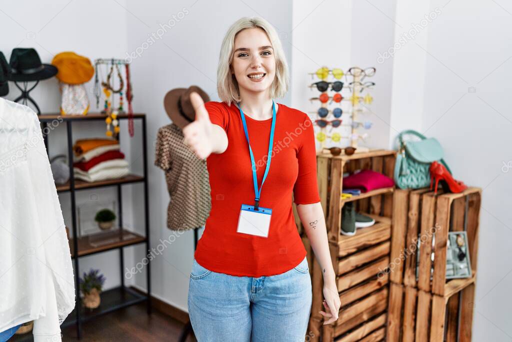 Young caucasian woman working as manager at retail boutique smiling friendly offering handshake as greeting and welcoming. successful business. 