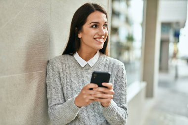 Genç İspanyol kadın şehirde akıllı telefon kullanarak mutlu bir şekilde gülümsüyor..