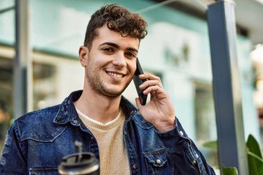 Genç İspanyol adam akıllı telefondan konuşuyor. Şehirde kahve içiyor.