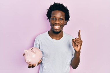 Genç Afrikalı Amerikalı adam elinde kumbarayla gülümsüyor bir fikri ya da sorusu olan mutlu bir yüzü olan bir adamı işaret ediyor. 