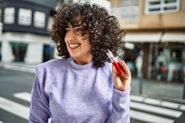 Orta Doğulu genç bir kadın gülümsüyor. Elinde elektronik sigara tutuyor.