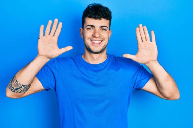 Günlük mavi tişört giyen genç İspanyol adam on numarayı gösterip işaret ederken kendinden emin ve mutlu gülümsüyor.. 