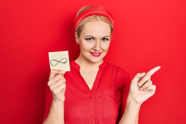 Sarışın genç kadın sonsuz bir sembol tutuyor. Gülümsüyor, mutlu bir şekilde işaret ediyor. 