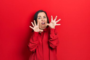 Orta yaşlı İspanyol kadın gündelik giysiler giyiyor. Korkudan dehşete düşmüş ve korkmuş. El hareketlerini durdur, şok içinde bağır. panik konsepti. 