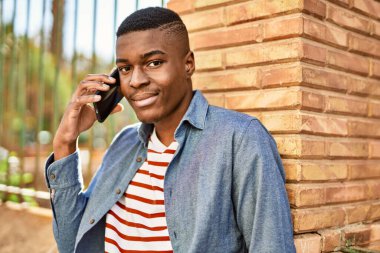 Genç Afrikalı Amerikalı gülümseyen mutlu bir adam şehirdeki akıllı telefondan konuşuyor..