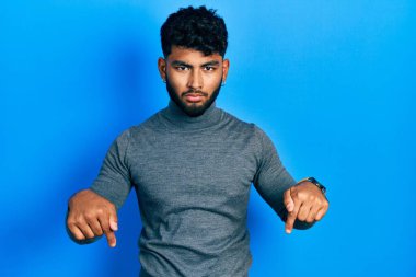 Balıkçı yaka kazak giyen Arap adam üzgün ve üzgün görünüyor, parmaklarıyla yön gösteriyor, mutsuz ve depresif.. 