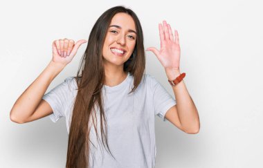 Gündelik beyaz tişört giyen genç İspanyol kız altı numarayı gösterip işaret ederken kendinden emin ve mutlu bir şekilde gülümsüyor.. 
