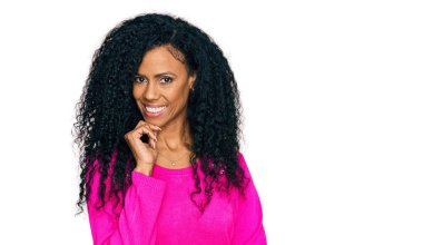 Orta yaşlı Afro-Amerikalı kadın günlük kıyafetler giyiyor kameraya özgüvenli bakıyor kollarını kavuşturup gülümseyerek ve çenesini kaldırarak. Olumlu düşünmek. 