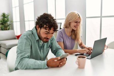 Laptop ve akıllı telefon kullanan genç bir çift evde kahve içiyor..