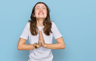 Young beautiful woman wearing casual white t shirt begging and praying with hands together with hope expression on face very emotional and worried. begging. 
