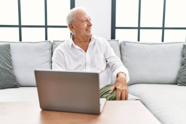 Sunbae evde dizüstü bilgisayar kullanıyor. Kanepede oturuyor. Yüzünde gülümseme ve doğal ifadeyle yan yana bakıyor. Kendinden emin gülen. 