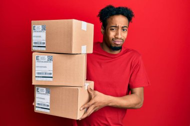 Sakallı, teslimat paketleri taşıyan, kafası karışık ve habersiz genç bir Afrikalı Amerikalı. şüphe kavramı. 