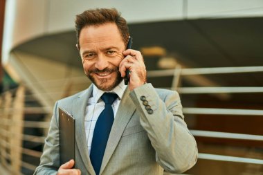 Orta yaşlı işadamı gülümsüyor. Şehirdeki akıllı telefondan konuşuyor..