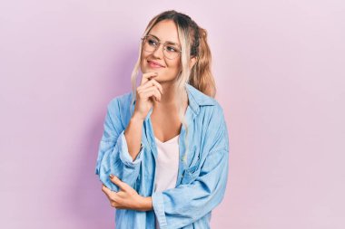 Gündelik kıyafetler ve gözlük takan güzel sarışın kadın kameraya kendinden emin bakıyor kollarını kavuşturmuş ve çenesini kaldırmış bir şekilde gülümsüyor. Olumlu düşünmek. 