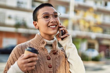 Kısa saçlı, gülümseyen, mutlu, kahve içen ve telefonda konuşan İspanyol bir kadın.