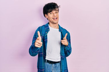 Yakışıklı, beyaz tişörtlü ve klasik tişörtlü genç adam kamerayı mutlu ve komik yüzüyle işaret ediyor. iyi enerji ve titreşimler. 