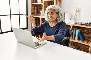 Orta yaşlı, gri saçlı, engelli bir kadın tekerlekli sandalyede otururken görüntülü konuşma yapıyor..
