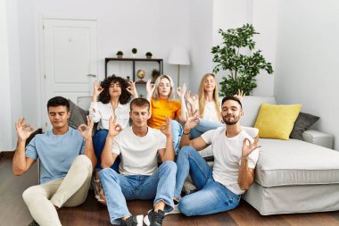 Bir grup insan kanepede oturup evde yerde rahatlar ve parmaklarıyla meditasyon yaparken gözleri kapalı gülümserler. yoga konsepti. 