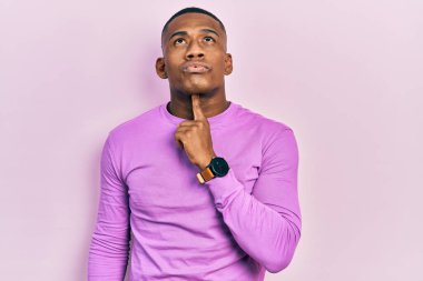 Genç siyah bir adam pembe bir süveter giyiyordu. Kuşku üzerine yoğunlaşmıştı. Parmakları çenesinde ve yukarı bakıyordu. 