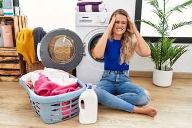 Genç ve güzel bir kadın hasır sepetin yanında oturmuş stres yüzünden başı ağrıyan elleriyle çamaşır yıkıyor. migren ağrısı. 