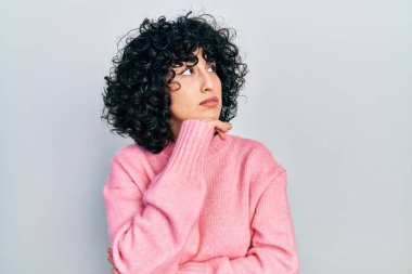 Orta Doğulu genç bir kadın. Elleri çenesinde gündelik kıyafetler giyip soru sormayı düşünüyor. Düşünceli bir ifade. Düşünceli bir yüzle gülümsüyor. şüphe kavramı. 