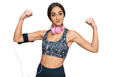 Güzel esmer kadın spor kıyafetleri giyip kulaklık takıyor ve gururla gülümseyen kol kaslarını gösteriyor. fitness konsepti. 