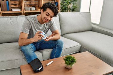 Evdeki kanepede oturan ve glikoz ölçen genç İspanyol diyabetik adam..