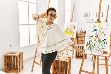 Genç İspanyol kadın sanat stüdyosunda müzik dinlerken kendinden emin bir şekilde gülümsüyor.