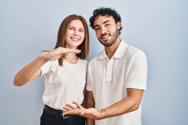 Gündelik giysiler giyen genç çift el ele tutuşup büyük ve büyük boy işareti ve ölçü sembolü gösteriyorlar. Kameraya bakıp gülümsüyor. ölçüm kavramı. 