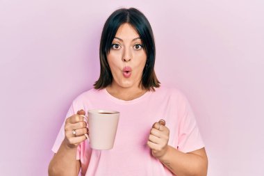 Genç İspanyol kadın bir fincan kahve içiyor. Korkmuş ve ağzı açık, şaşırmış ve şaşırmış. 