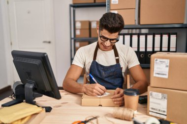 Latin kökenli genç bir iş adamı iş yerinde paket üzerine yazıyor.