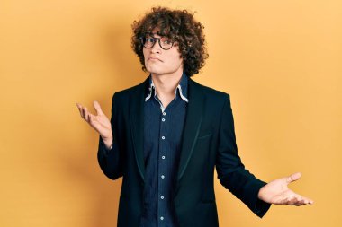 İş ceketi giyen yakışıklı, gözlüklü, kafası karışık, elleri ve kolları havada genç bir adam. şüphe kavramı. 